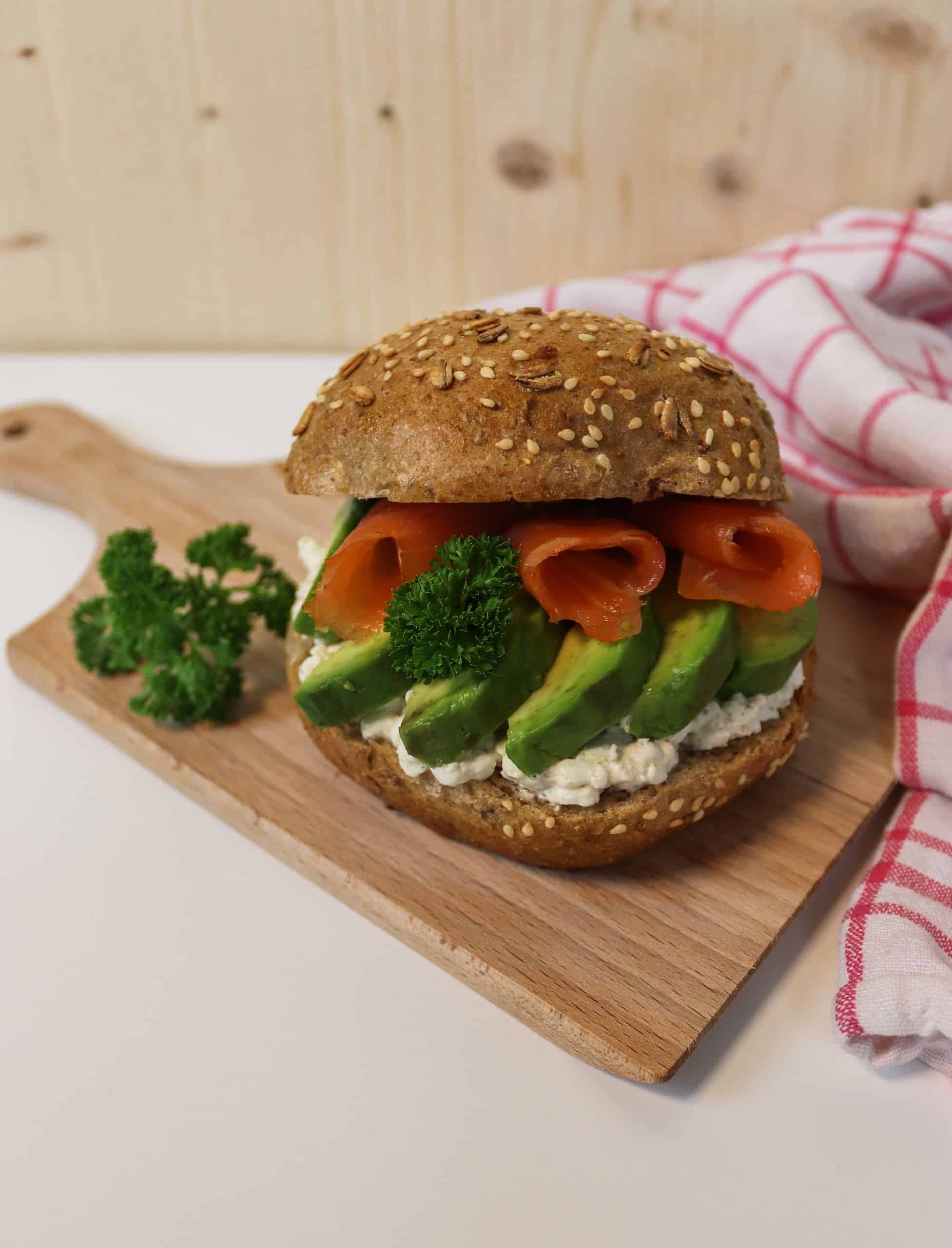 Leckeres Vollkornbrötchen mit Lachs, Avocado und Frischkäse auf einem Brett