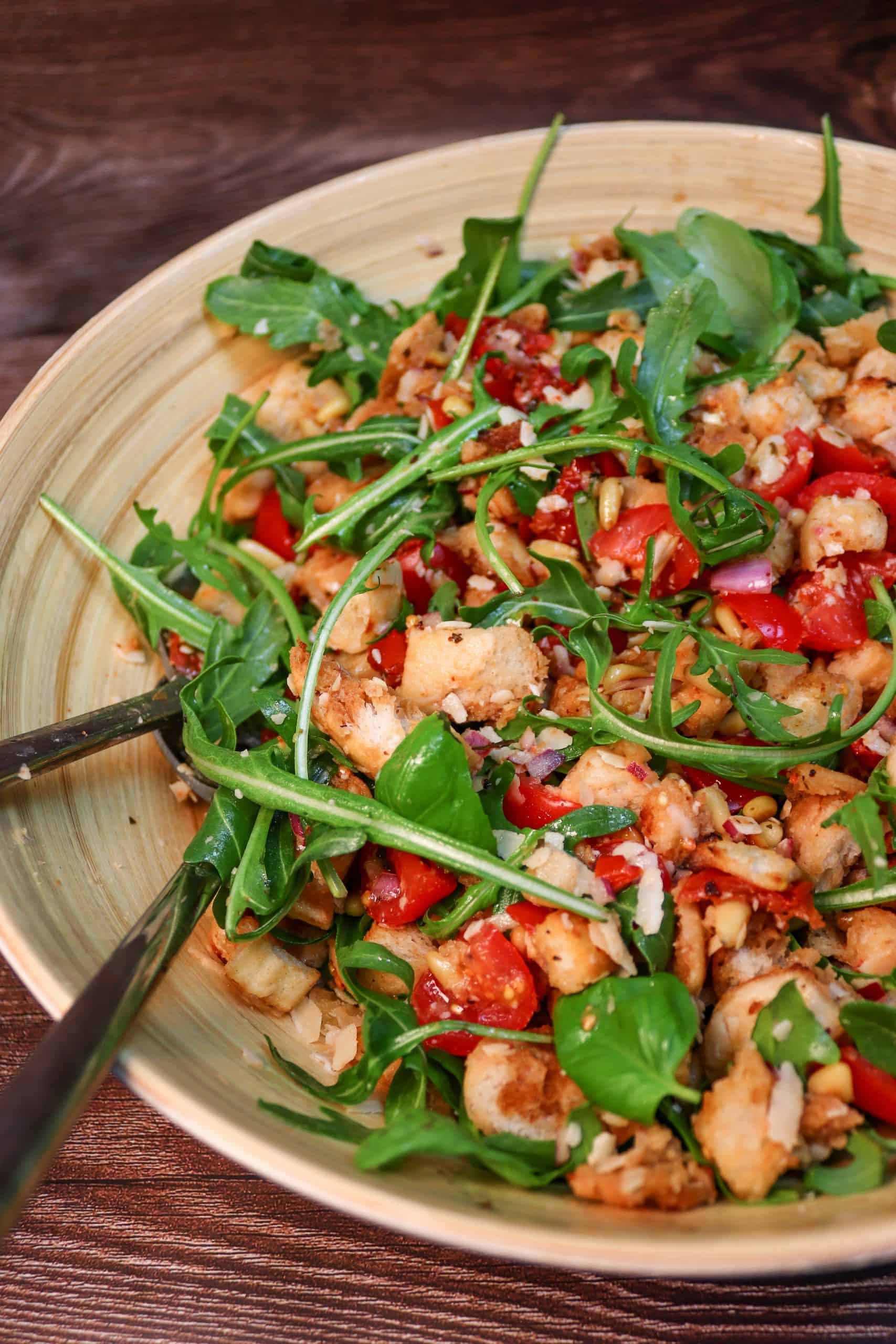 Leckerer Brotsalat mit Tomaten und Rucola in einer Salatschüssel auf einem Tisch