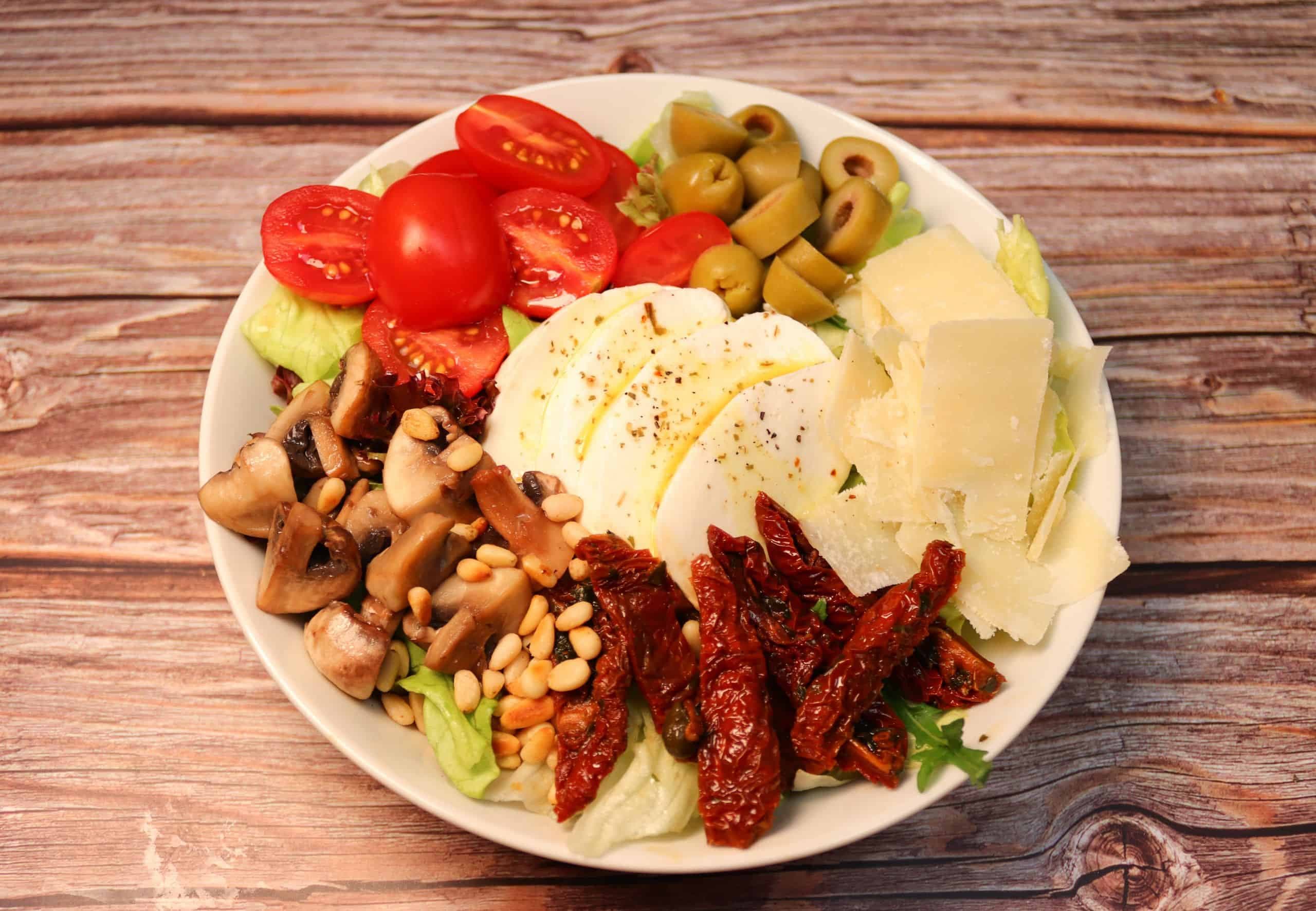 Antipasti Salat Bowl mit Tomaten, Oliven, Pilze, Mozzarella, Parmesan und Pinienkernen