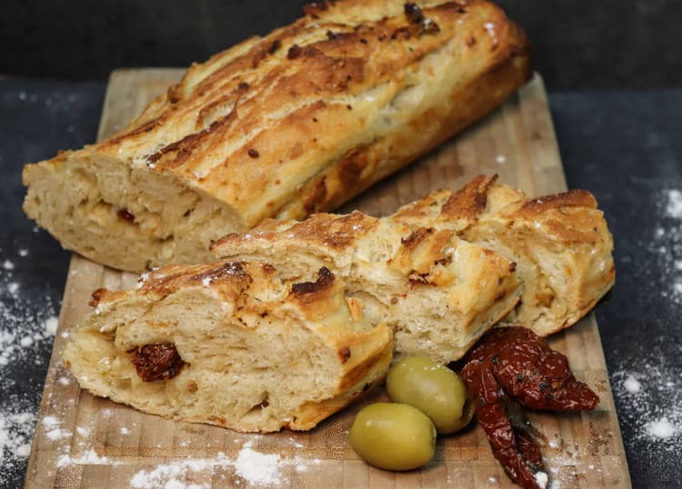 Leckeres mediterranes Baguette mit getrockneten Tomaten und Oliven auf einem Brett.