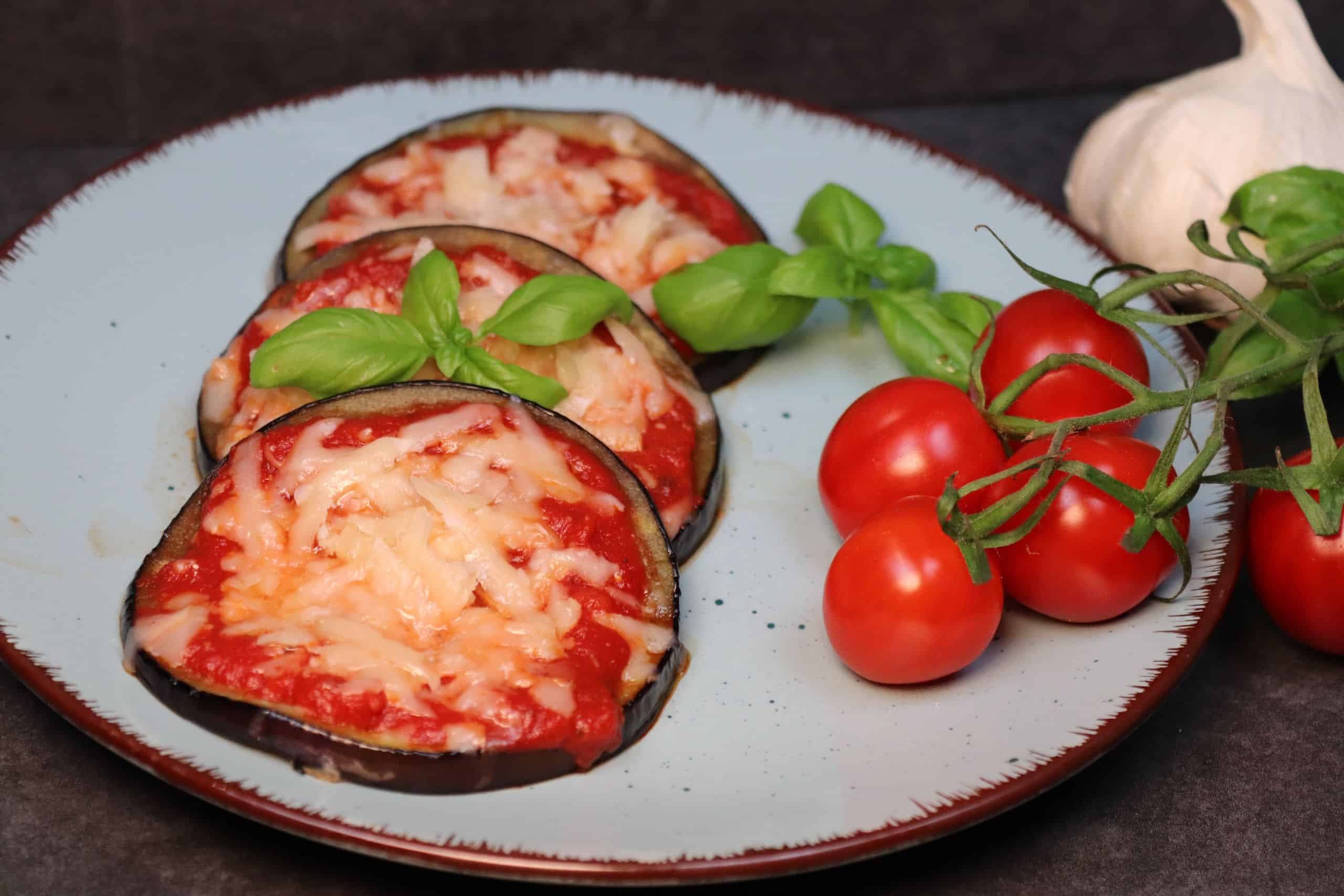 Drei leckere Mini-Auberginen-Pizzen mit Cocktailtomaten auf einem Teller.