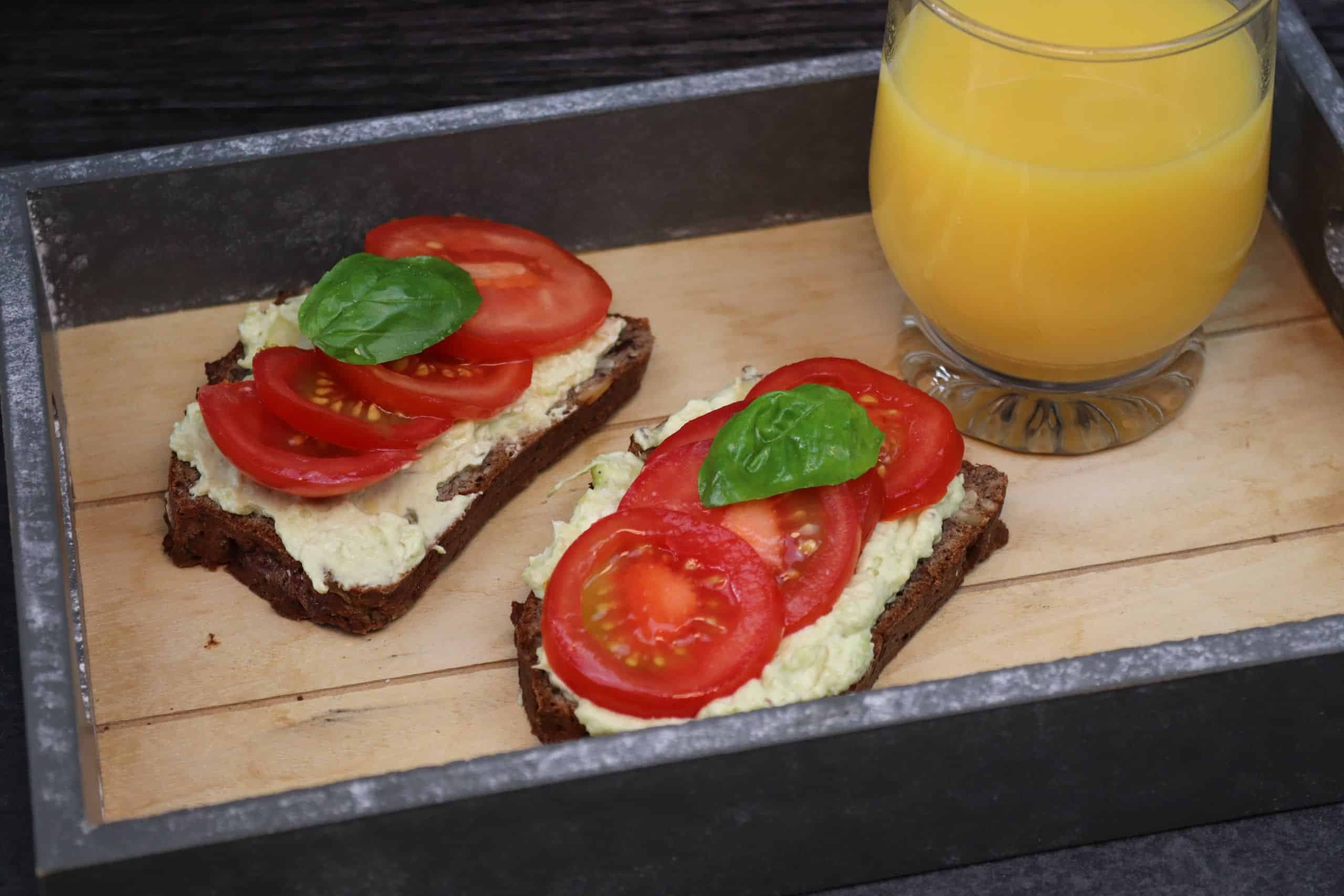 Leckere Avocado Sandwich mit Tomaten und einem Basilikumblatt auf einem Tablett mit einem Glas Orangensaft.