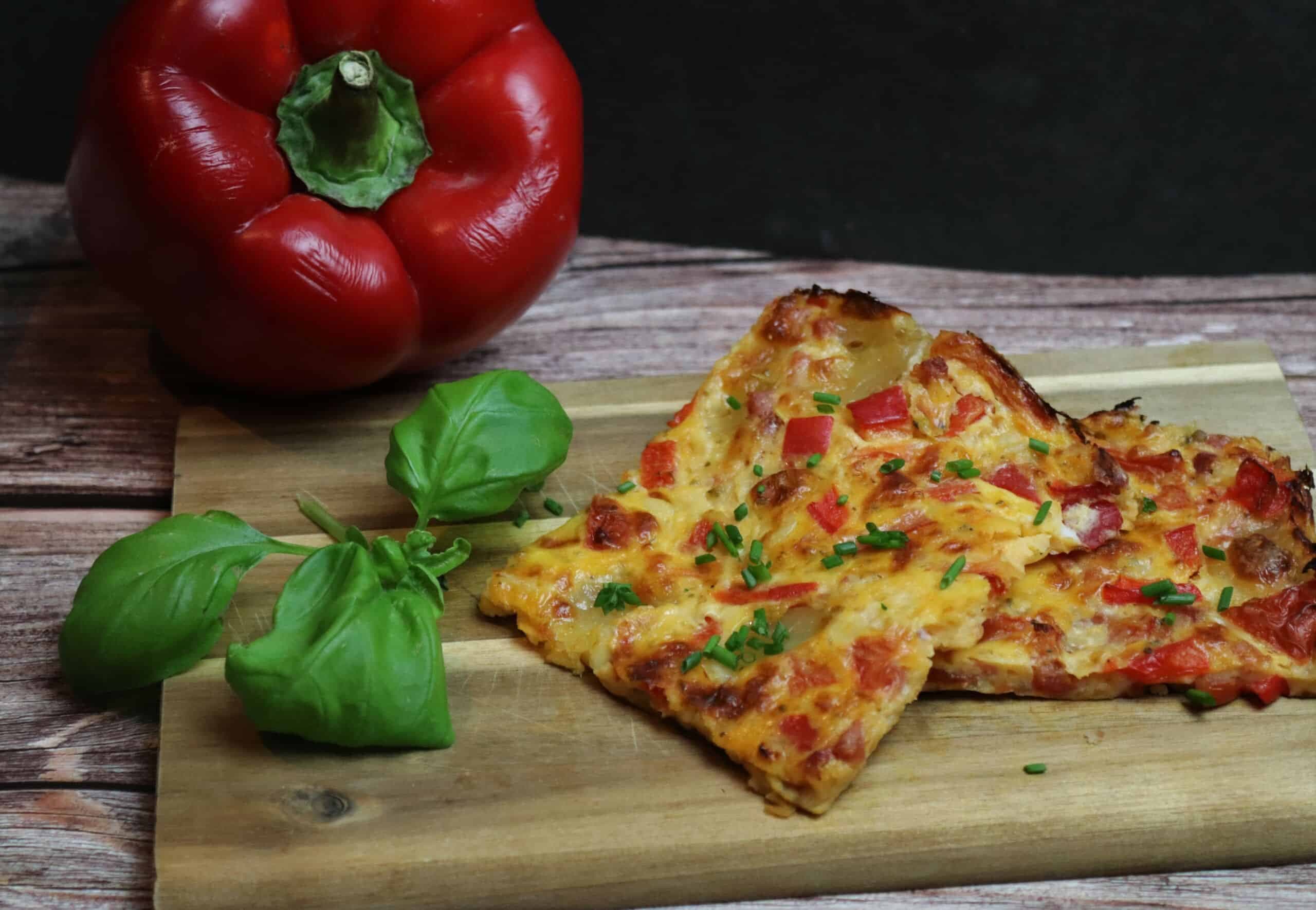 Low-Carb Pizza auf einem Brettchen mit Paprika und Basilikum