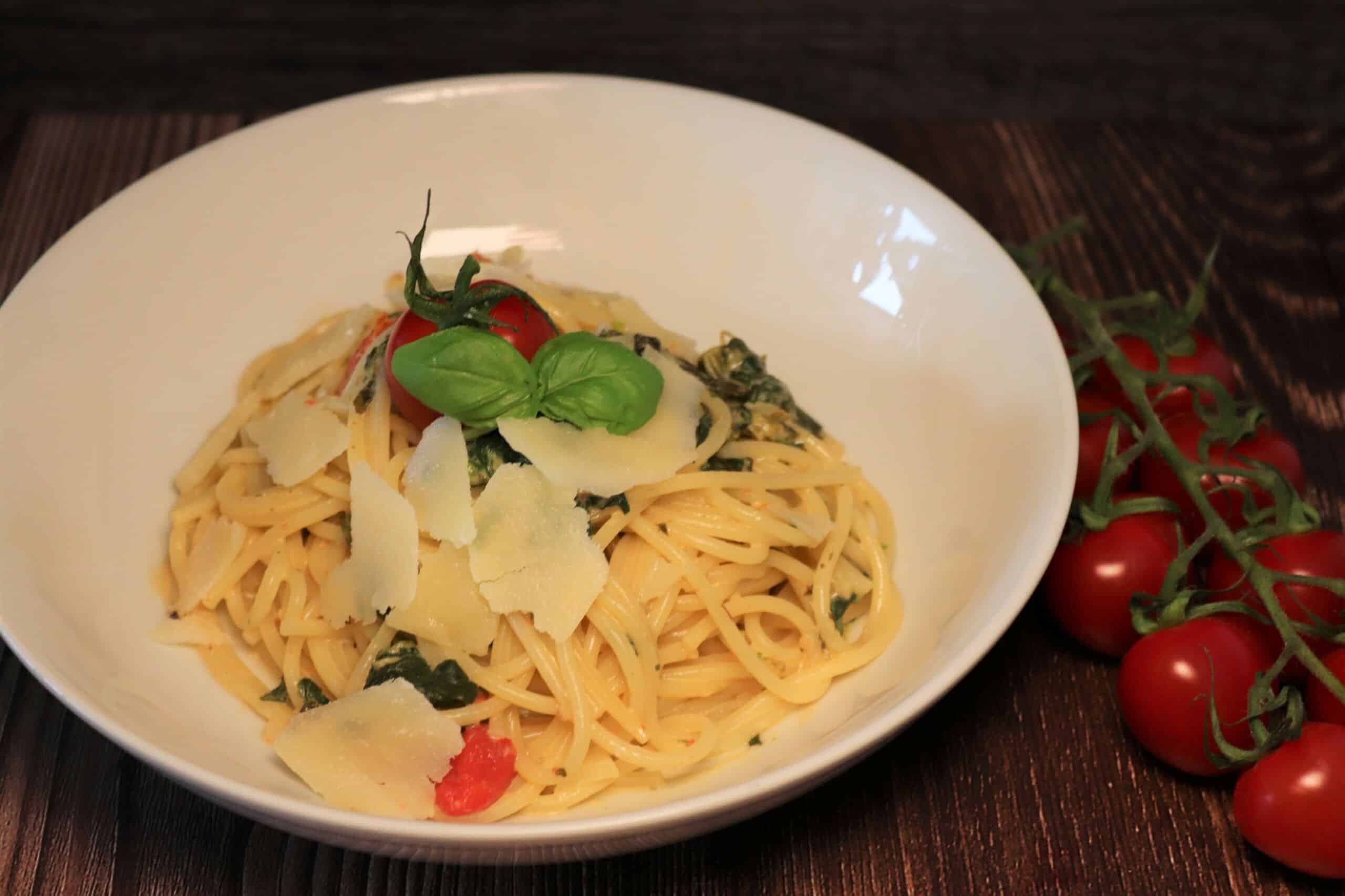 Leckere Spinat-Tomaten-Frischkäse-Pasta mit Parmesan und Basilikum in einem Teller