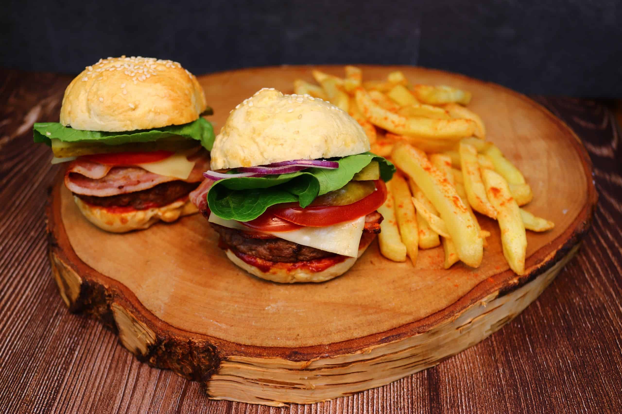 Leckere selbstgemachte Burger mit Pommes auf einer Holzscheibe.