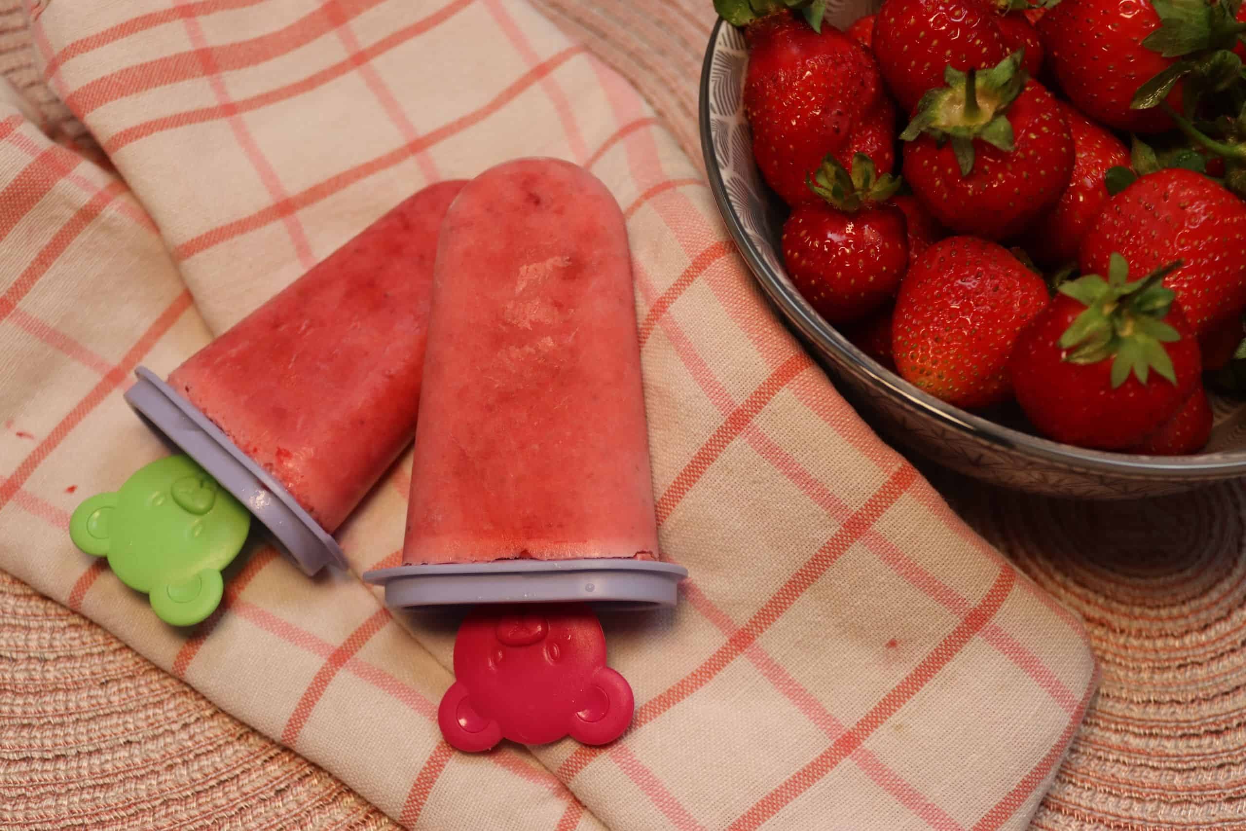 Leckeres Erdbeer-Jogurt-Eis auf einem Küchentuch und mit einer Schüssel Erdbeeren daneben.